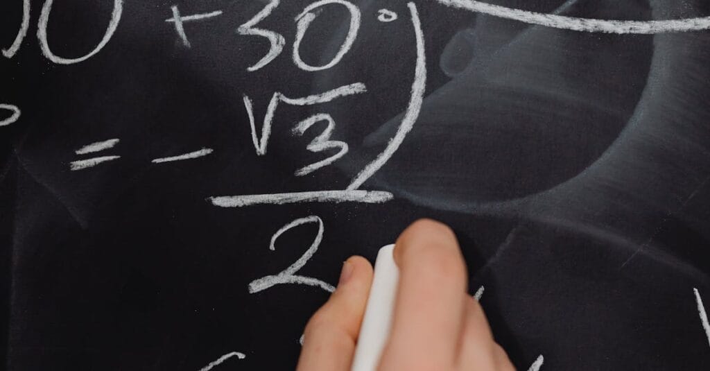 Hand writing complex math equations on a blackboard in a classroom setting.